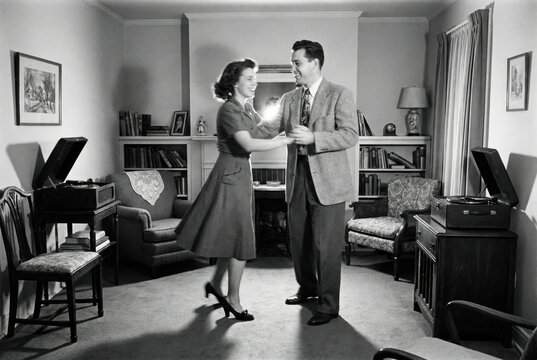 A black and white vintage photograph of a happy couple dancing in their living room in the 1940s or 1950s.