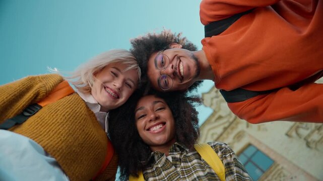 Three multiracial students leaning heads together celebrate success looking down bottom view in city university African American man male guy Caucasian women girls females education winners gesture