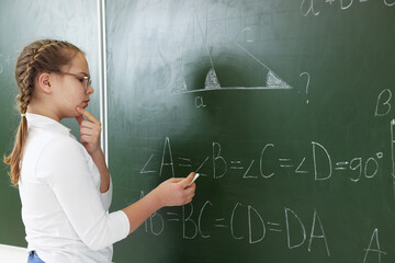 Schoolgirl doing math on chalkboard in classroom