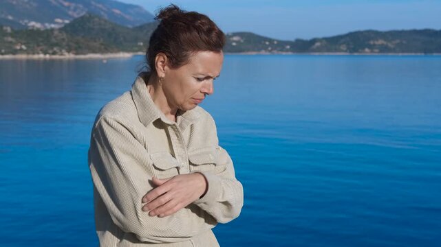 Sad woman reflecting by the sea: expressing despair and loneliness. Woman standing by sea, arms crossed, head lowered, embodying deep emotional struggle with profound sense of isolation and inner pain