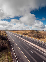 Two lane on each side freeway with fine asphalt surface, country side with green fields on each side. Cloudy sky. Commercial motor way with high speed. Transportation industry. Travel and tourism.