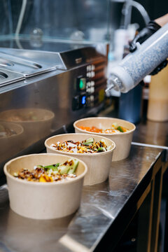 Sauce being poured over takeaway salad bowls on stainless counter in restaurant kitchen