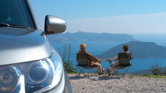 Senior couple finishing their picnic by the sea. Mature man and woman packing up their folding chairs after enjoying a scenic picnic stop during a road trip, with a stunning view of the ocean bay