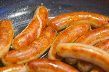 Fototapeta premium Golden brown sausages cooking in a pan with sizzling oil