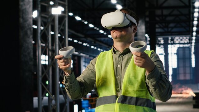 Industrial worker with VR glasses interacting with virtual reality simulation used for engineering development, surrounded by metal machinery and fabrication tools in industry plant.