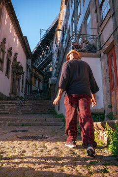 Person walking up a traditional cobblestone street, climbing stone steps in Porto with Dom Lu&iacute;s I Bridge visible in the background.