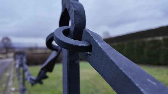 Close-up of ornate wrought iron gate detail. Focus shifts across the Celtic knot design. Background shows a rural landscape with a road and greenery. The video pans slowly along the fence line