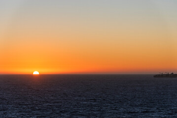 Fototapeta premium Dramatic sunset sky above the Pacific Ocean with vessel silhouetted against the horizon.