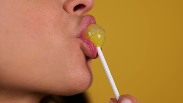 Young woman sexy eating chupa chups, close up. Woman lips sucking lollipop. Sensual concept. Copy space. Isolated yellow background. Real time