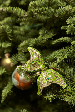 Green sequined butterfly ornament adorns fresh evergreen Christmas tree branches with festive holiday sparkle