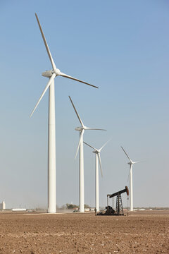 White wind turbines stand alongside an oil pump jack in an arid desert landscape