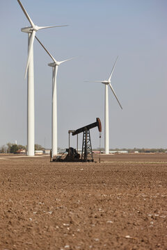 Wind turbines and oil pump jack demonstrate renewable and fossil fuel energy sources in rural landscape