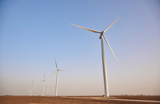 Wind turbines generating renewable energy in an open agricultural field under clear blue sky