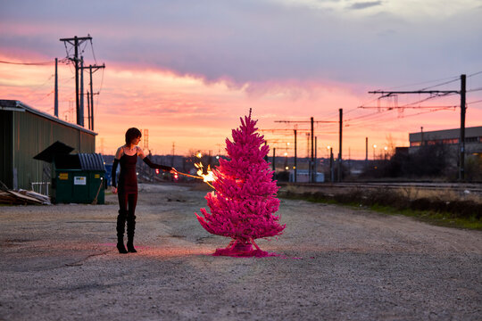 Woman sets fire to pink painted Christmas tree in industrial parking lot at sunset