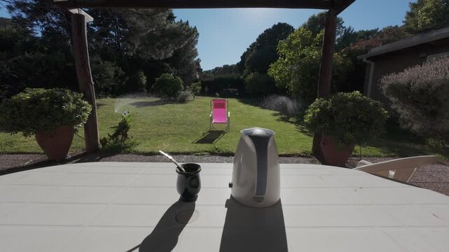 Mate tea ceremony set on a table in a sunny garden with sprinklers watering the green grass. 4K