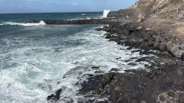 Powerful Atlantic surf crashes into black volcanic rocks along a rugged island shoreline under dramatic clouds. Natural seascape with white foam, spray, and deep blue water.