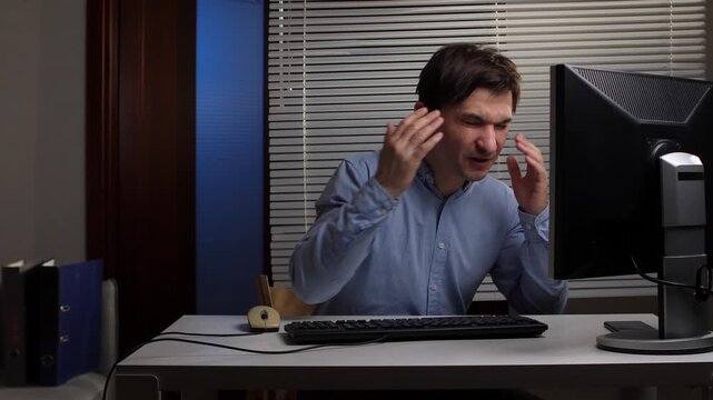 Angry man sitting at his office desk, yelling and gesturing wildly at his computer screen, expressing frustration and experiencing high stress from a technical error or demanding work