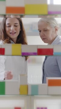 Female pharmacist giving medicine box to senior woman with prescription on smartphone at pharmacy
