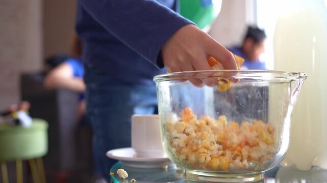 Close up of a popcorn bowl as a little girl reaches in, grabs a handful, and returns to her seat. Cozy soccer match night at home with family and friends