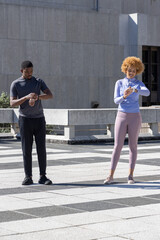 Obraz premium Male and female sporty friends checking and adjusting wrist devices on plaza near concrete railing