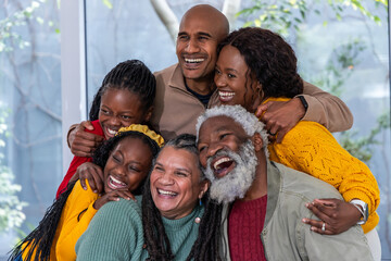 African American family laughing, hugging at home by large glass window, knit sweaters, watch seen