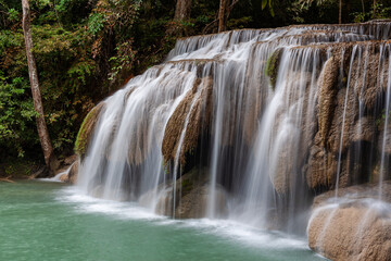 Fototapeta premium Erawan Waterfall cascading down rocky terrain in Erawan National Park, Kanchanaburi, Thailand. Lush green forest surrounds the clear water stream.