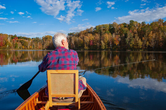 Senior man trout fishing in a wooden canoe on a calm northern Minnesota lake on a beautiful autumn day