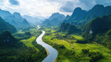 Majestic river winds through lush green valley surrounded by dramatic mist-shrouded mountains under a cloudy sky