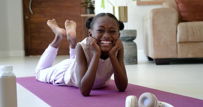 African child lying on purple mat in living room, responding to camera, smiling near headphones