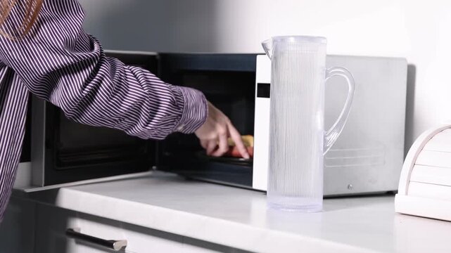 Woman putting plate with rice and chicken into microwave in kitchen, closeup. Camera moving forward