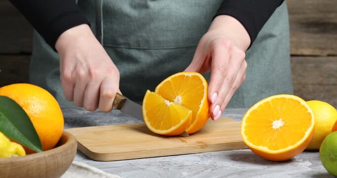 Woman cutting fresh orange at grey table, closeup