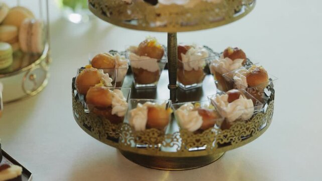 Elegant dessert stand with mini pastries and cream at wedding reception, luxury candy bar with bite-size sweets on vintage tiered tray, stylish celebration catering detail
