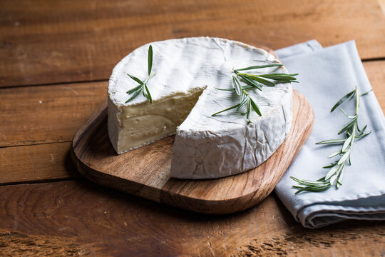 Camembert or brie cheese served on a rustic wooden table, natural light, artisanal food styling and simple composition.