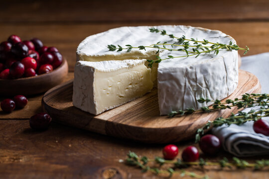 Camembert or brie cheese served on a rustic wooden table, natural light, artisanal food styling and simple composition.