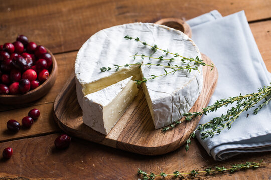 Camembert or brie cheese served on a rustic wooden table, natural light, artisanal food styling and simple composition.