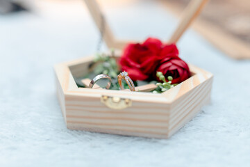 Elegant wedding rings and roses in wooden gift box on soft fabric