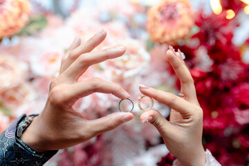 Hands holding wedding rings with beautiful floral background