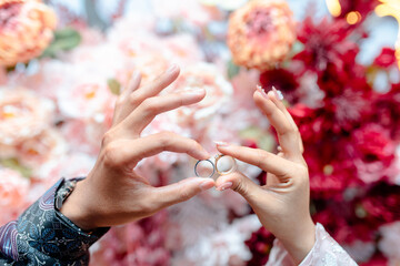 Couple's hands holding wedding rings in front of beautiful floral background