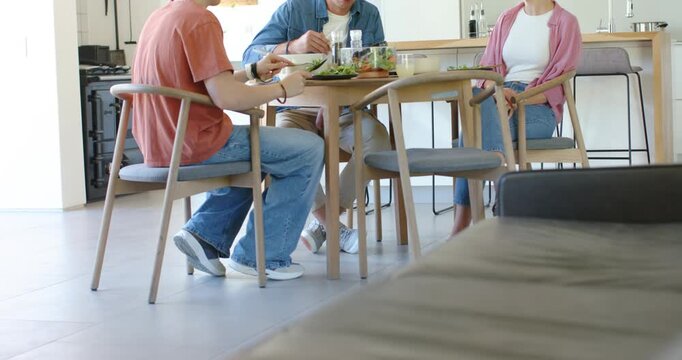 Family at dining table sharing meal, man serving salad while woman speaking, teenage son listening