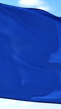 A plain blue flag waves gracefully in the gentle breeze against a clear blue