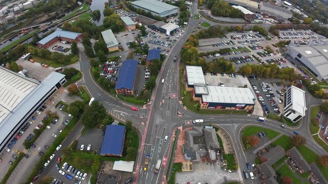 Aerial Retail Campus And Roundabout Leeds, Busy Junction With Parking Lots, Bus Stops, Pedestrian Crossings And Blueroofed Stores, Cars And Buses Moving Through Commercial Hub Under Soft Daylight