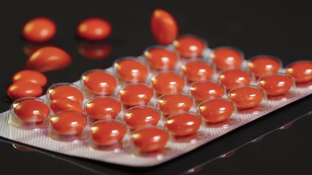 Red Sugar-Coated Pills tablets falling onto blister pack and colliding suggesting medication or medicine pharmaceutical themes, health, healthcare, treatment, and medical care