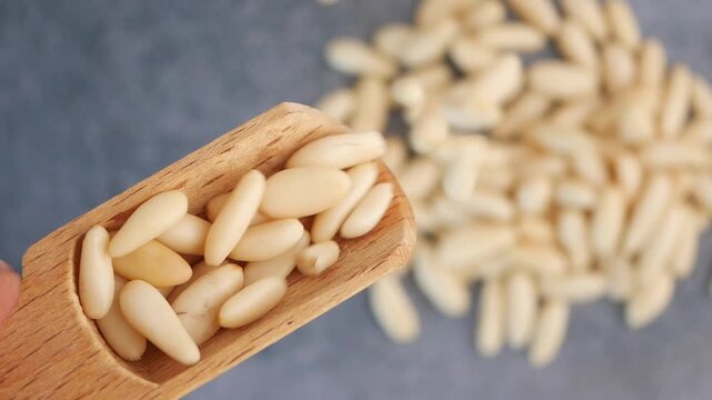 Slow motion video of pine nuts falling from wooden scoop onto gray stone background