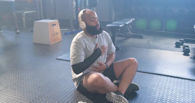African American man placing hands on chest and stomach doing breath control at gym wearing headset