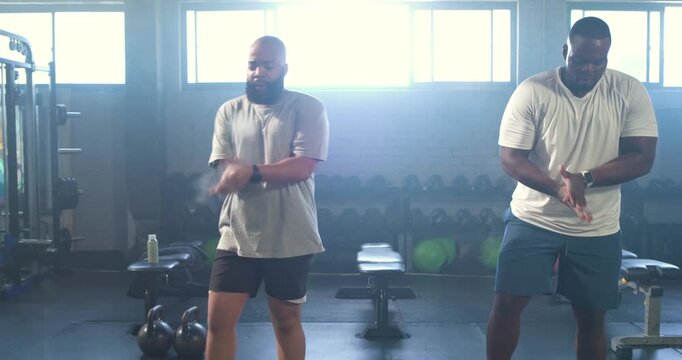 Two male workout partners nodding, warming up, picking kettlebells and swinging for strength at gym