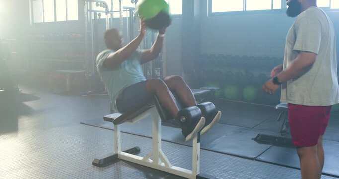 African American trainer starting green ball pass as trainee doing situps on decline bench for core