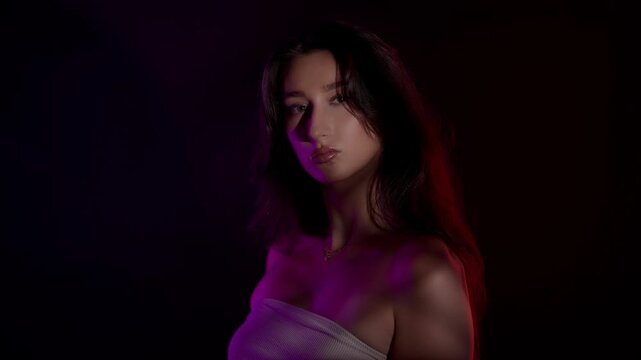 Slow motion beauty shoot of a sensual brunette model with perfect skin in a studio setting The model is posing with dramatic red and purple lighting creating a seductive and elegant atmosphere for fas