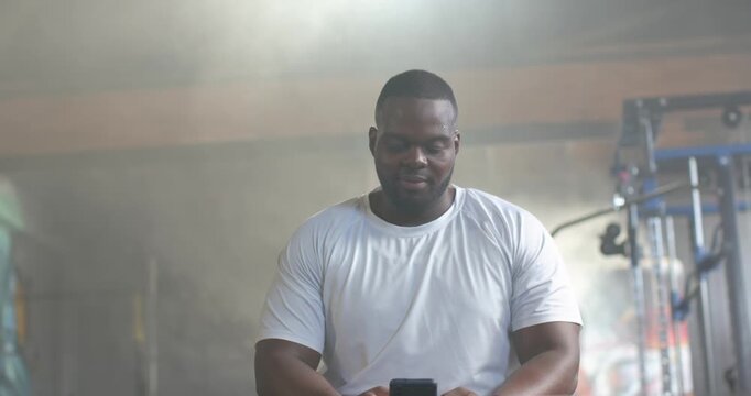 Muscular man noticing phone on bench, grabbing it and checking messages near cable machine in gym