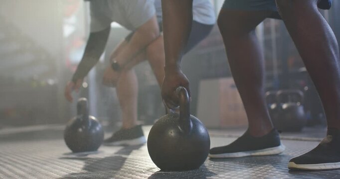 Two African American men chalking hands then swinging kettlebells in gym in shorts for strength