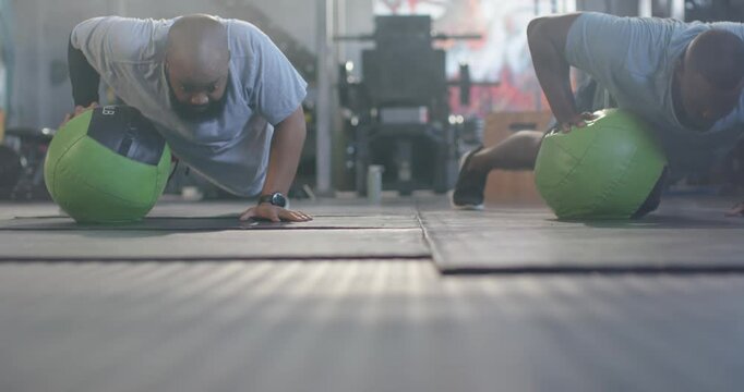 Two African American men starting plank holding 14LB medball switching pushups at gym for core